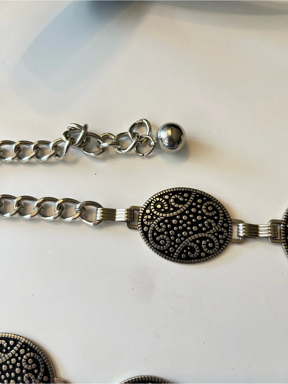 Silver-tone chain belt features textured medallion links and a hook closure L/XL